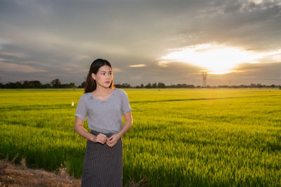 Young woman standing on agricultural field against sky during sunset