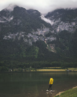 Full length of man standing on rock in lake against mountain
