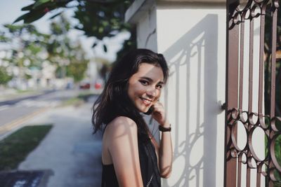 Portrait of young woman standing by fence