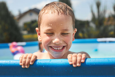 Portrait of happy smiling boy playing in a pool having fun on a summer sunny day