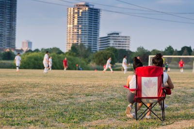 Rear view of women sitting on deck chair while looking at people playing