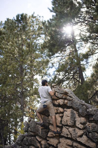 Rear view of hiker climbing rock formation against trees at forest