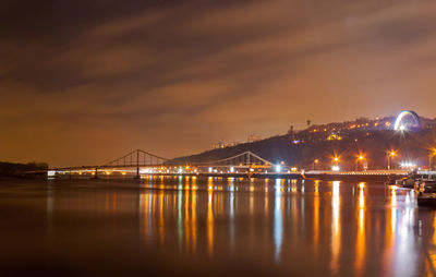 Illuminated bridge over river against sky at night