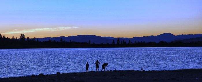 Silhouette people standing by lake against sky during sunset