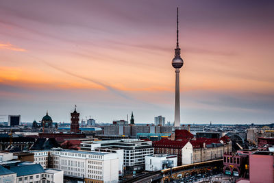 Communications tower in city against sky during sunset