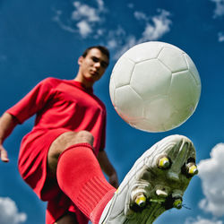 Low angle view of young man playing soccer against blue sky