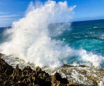 Waves splashing on rocks at shore against sky