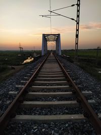 Surface level of railroad tracks against sky during sunset