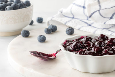 A bowl of sweet blueberry sauce with fresh blueberries in behind.