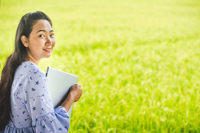 Portrait of woman holding laptop while standing on field