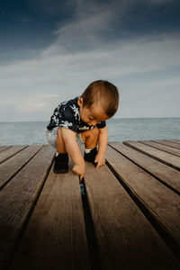 Full length of boy sitting on wood against sea