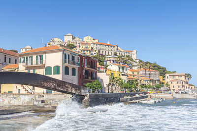 Buildings by sea against clear blue sky