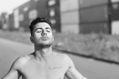 Close-up of shirtless young man with eyes closed standing on road during sunny day