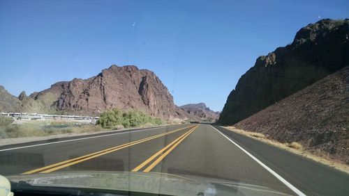 Street amidst mountains seen through windshield