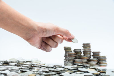 Close-up of hand holding coin stack against white background