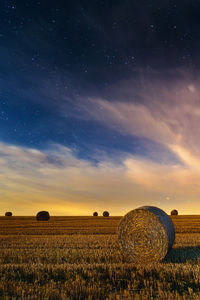 Hay bales on field against sky during sunset