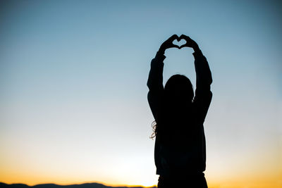 Silhouette woman standing by heart shape against sky during sunset