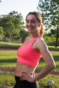 Portrait of happy female athlete standing by running track on field