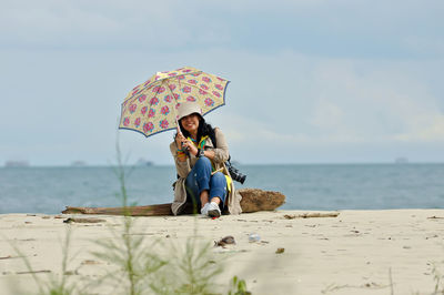 Woman with umbrella on beach against sky