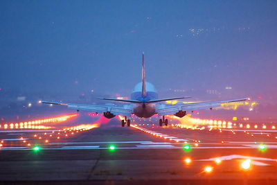 Airplane flying over runway against sky at night