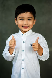 Portrait of cute boy showing thumbs up against gray background