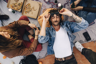 Directly above shot of man holding sunglasses while lying down amidst friends in party on rooftop