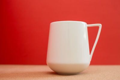 Close-up of coffee cup on table against red background