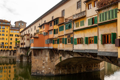 Arch bridge over river by buildings in city against sky