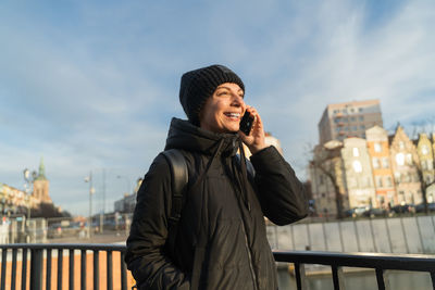 Smiling young woman talking on smartphone. travel blogger with backpack walking on the city street.
