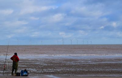 Full length on man standing by fishing rod on beach