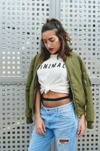 Fashionable young woman standing against gray trellis