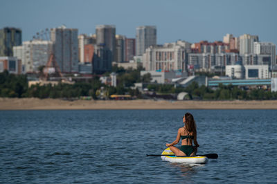 Rear view of woman sitting on paddleboard in sea