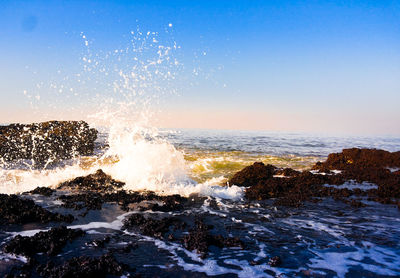 Waves splashing on rocks against clear blue sky