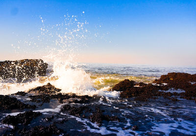 Waves splashing on rocks against clear blue sky