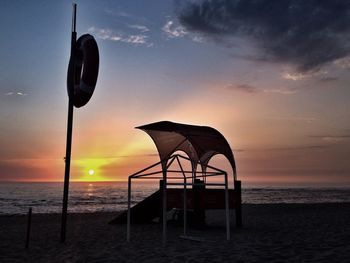 Silhouette lifeguard hut on beach against sky during sunset