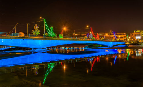 Illuminated bridge over river against sky at night