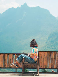 Rear view of woman sitting on bench against mountain