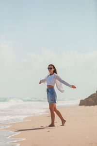 Full length of young woman standing at beach against sky