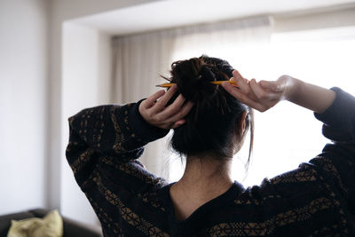 Woman tying hair with pencil at home