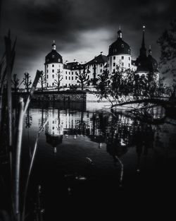 Illuminated building by river against sky in city