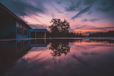Reflection of trees and house in lake against sky during sunset