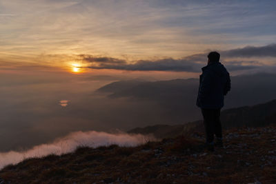 Rear view of man standing on mountain against sky during sunset