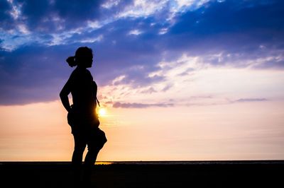 Silhouette of people standing on landscape at sunset