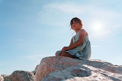 6 years old girl sitting on rock against sky