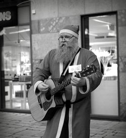 Man in santa costume playing guitar while standing on sidewalk