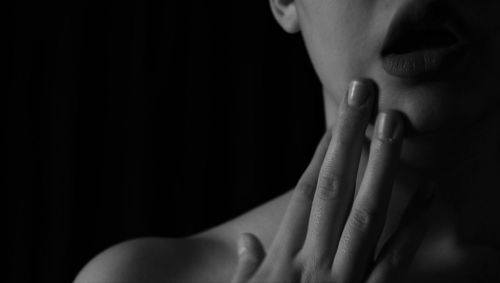 Midsection of woman touching chin against black background