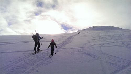 Father and daughter skiing on snowcapped landscape against sky