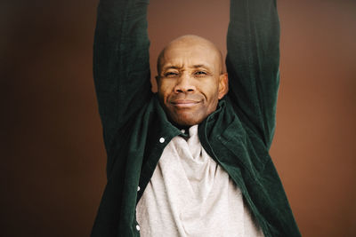 Mature man with arms raised over brown background in studio