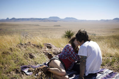 Couple kissing while sitting on field against clear sky