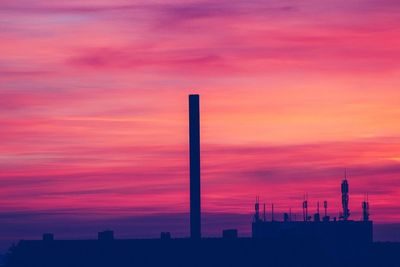 Silhouette of factory against orange sky
